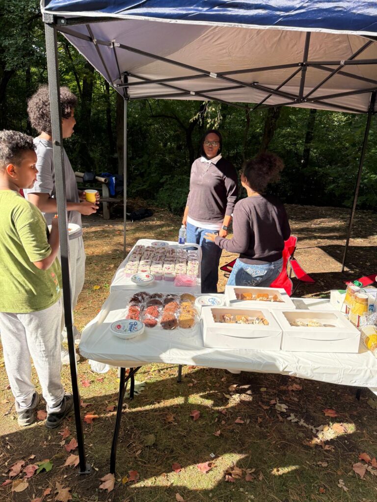 People setting out food and refreshments on tables at an outdoor event.
